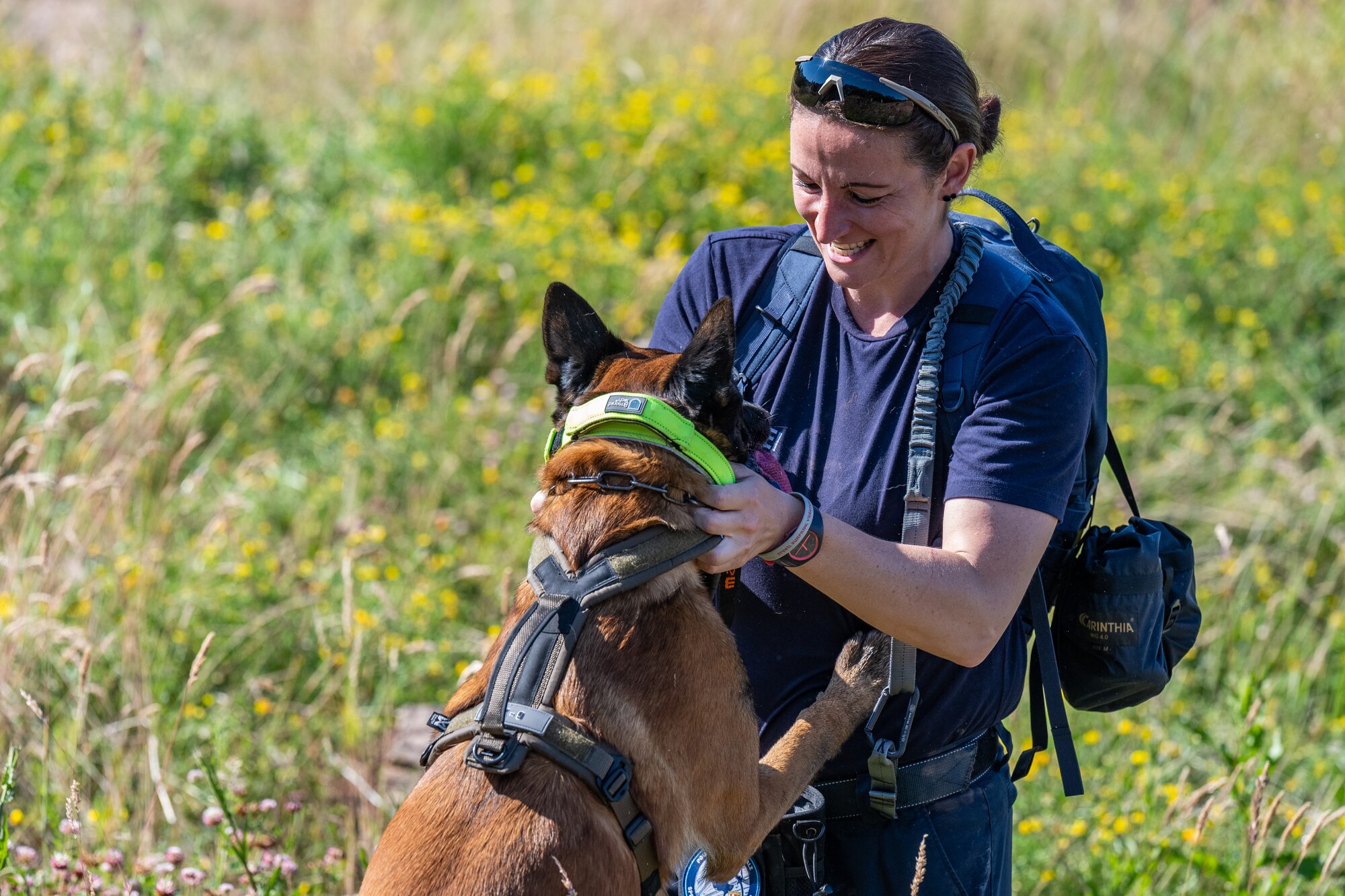 A working dog handler smiles and pets her working dog as it jumps on her.