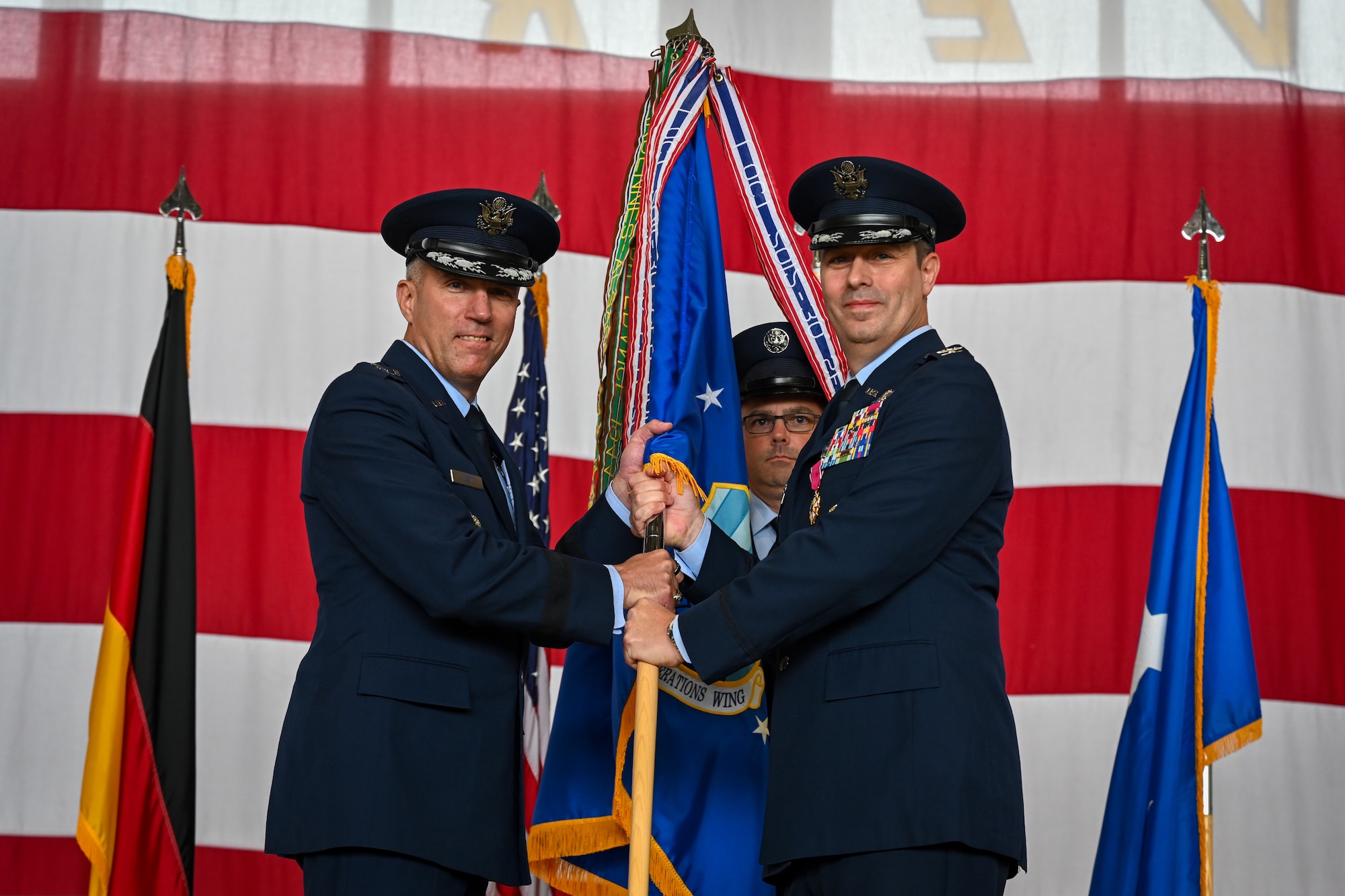 Col. Dan Cooley (right), outgoing 521st Air Mobility Operations Wing commander, relinquishes the guidon to Maj. Gen. John Klein, U.S. Air Force Expeditionary Center commander, during a change of command ceremony at Ramstein Air Base, Germany, July 3, 2024.