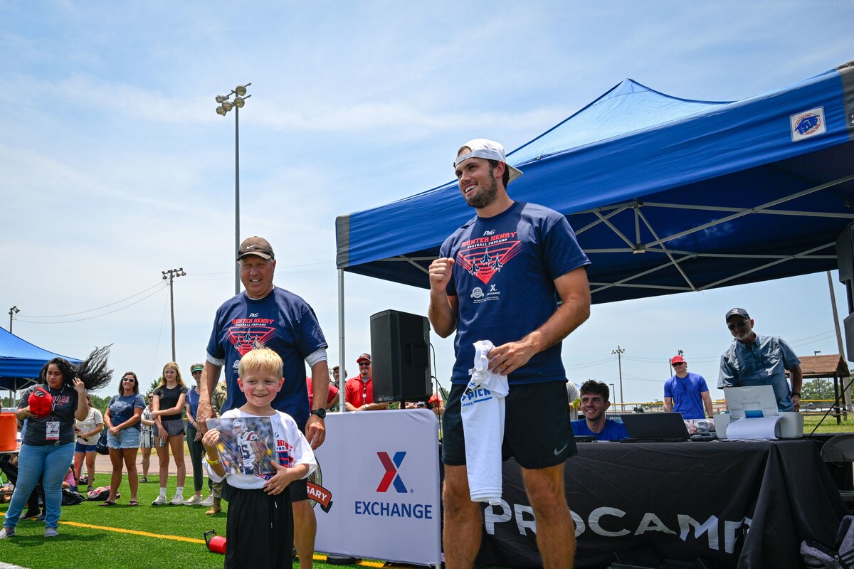 A man wearing a blue shirt gives a child wearing a white shirt an autographed photo during a football camp.