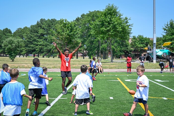 A coach wearing a red shirt raises his arms to celebrate during a football camp.