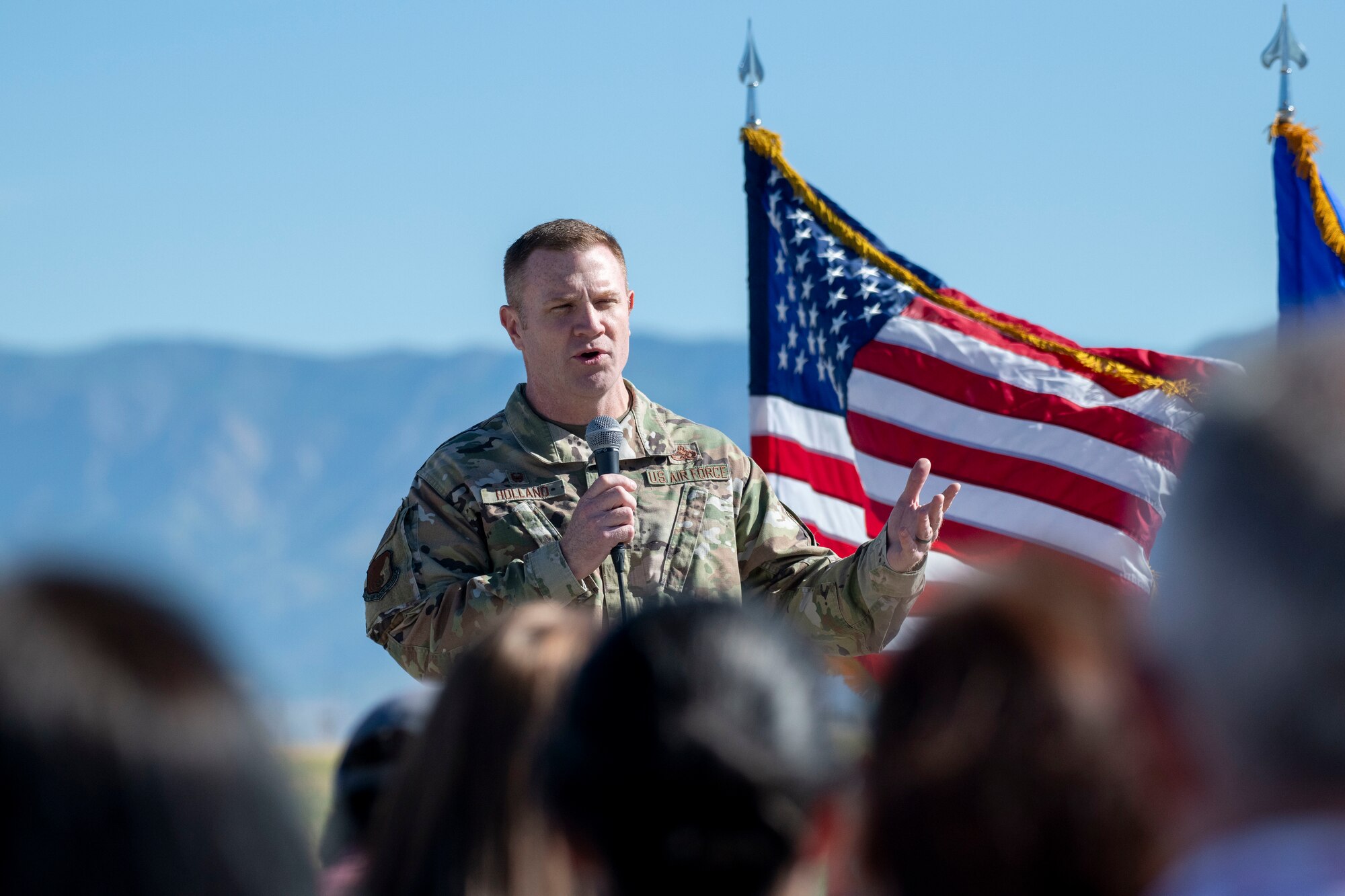 Col. Hollands speaks to attendees seated on the airfield.