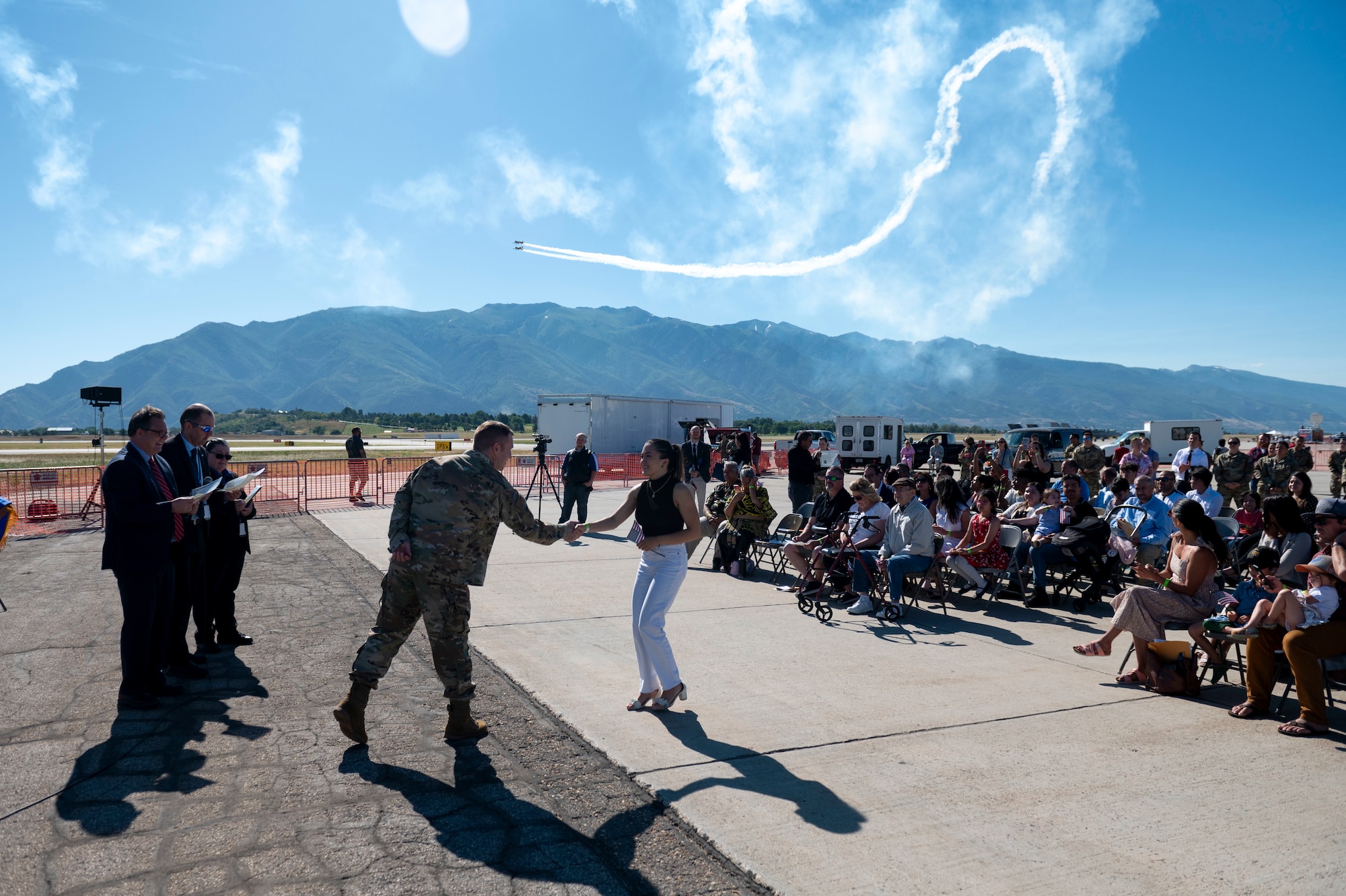 Col. Holland shake the hand of a new U.S. citizen. A plane practicing for the air show can be seen flying in the sky in the background.