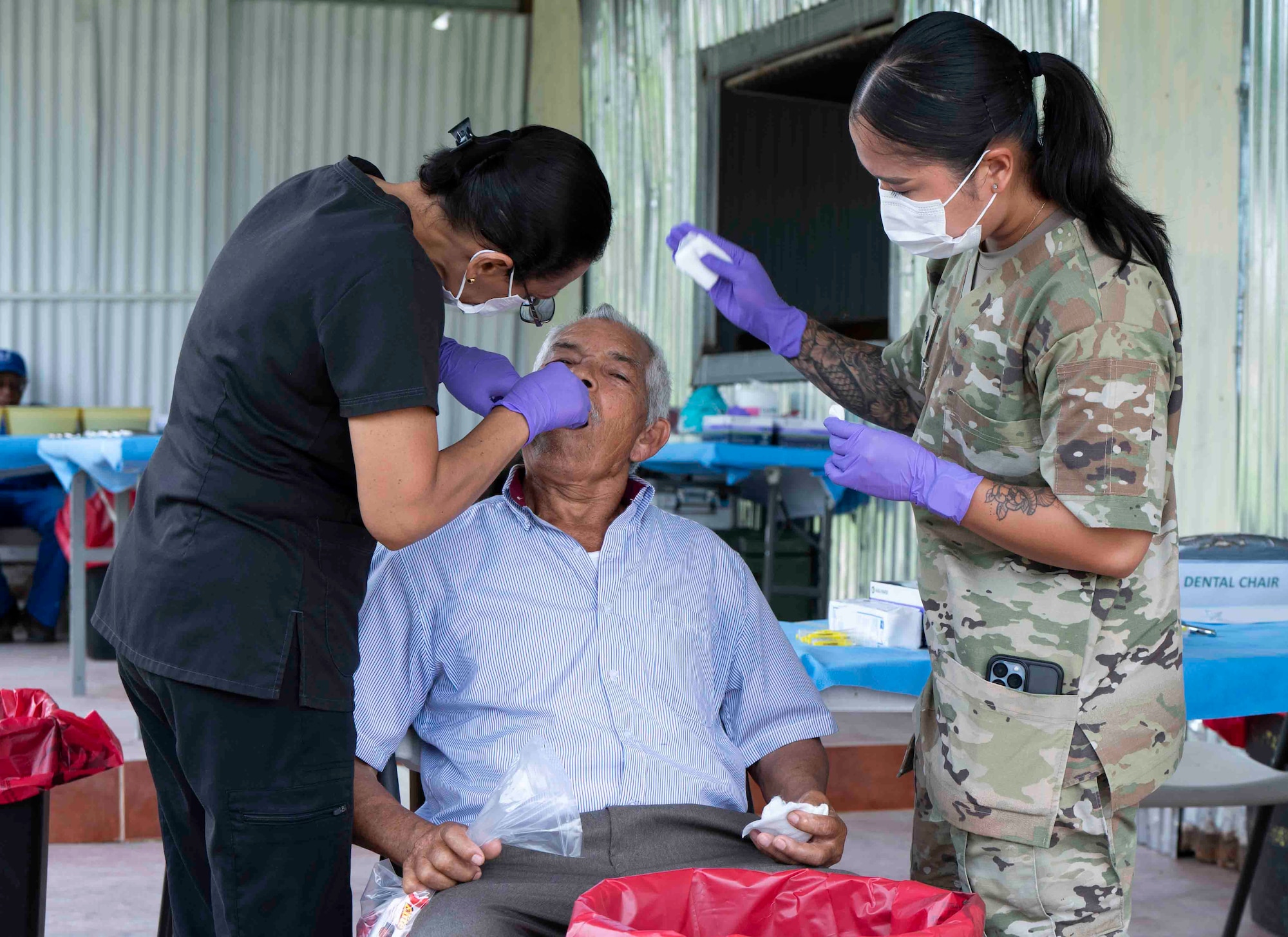 A photo of a military medical professional assisting another while they extract a patient's tooth.