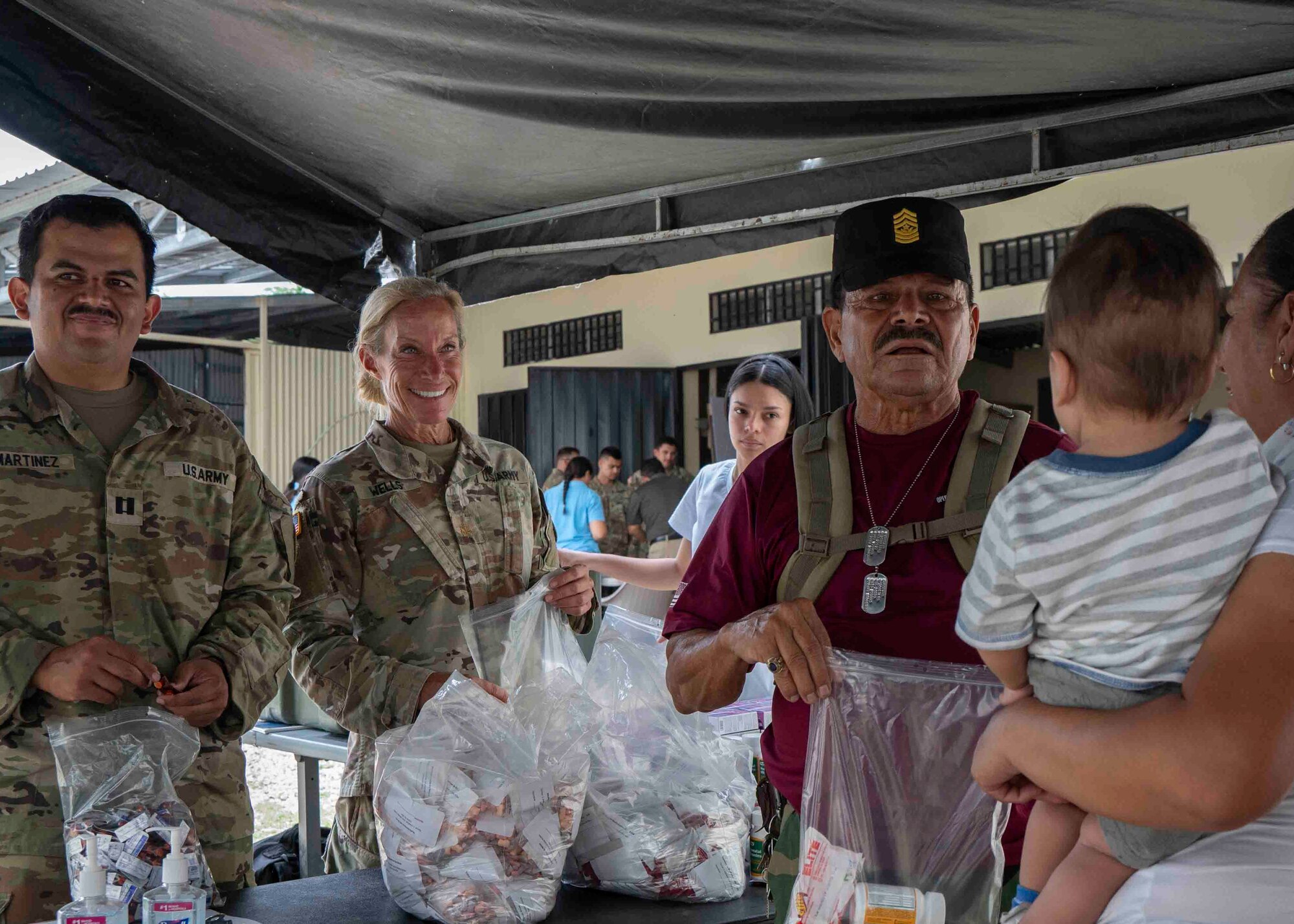 A photo of two military members waiting to fill a bag with preventive medicine supplies for a patient and her child.