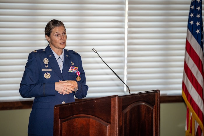 Lt. Col. Justus gives a speech while standing behind a podium, an American flag fills right side of image