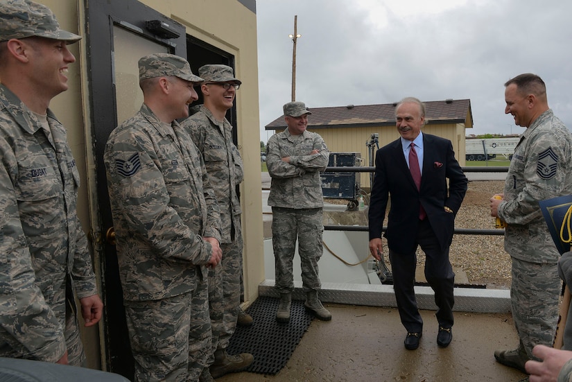 A person dressed in civilian clothing talks to a group of service members. All are standing outside a building.