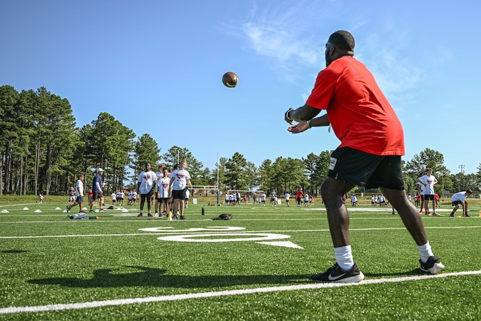 A coach wearing a red shirt prepares to catch a football from one of the children during a football camp.