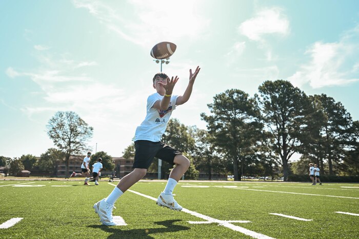 A child wearing a white shirt catches a football on a turf field