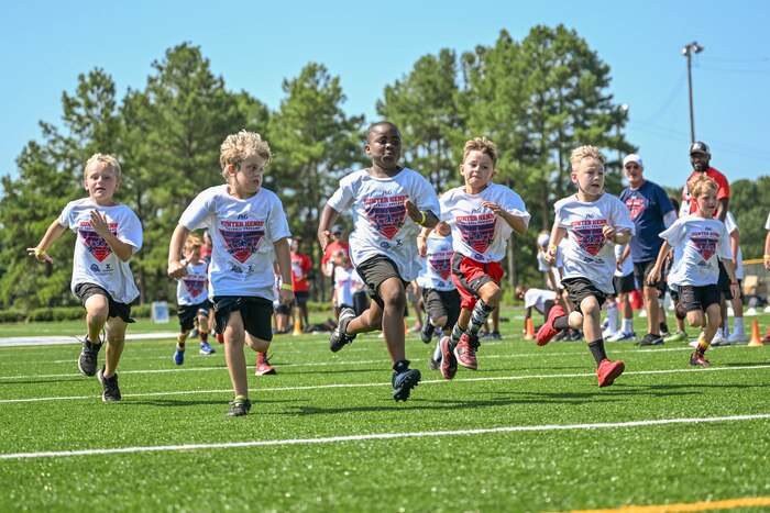 Multiple children wearing white shirts race during a football camp.