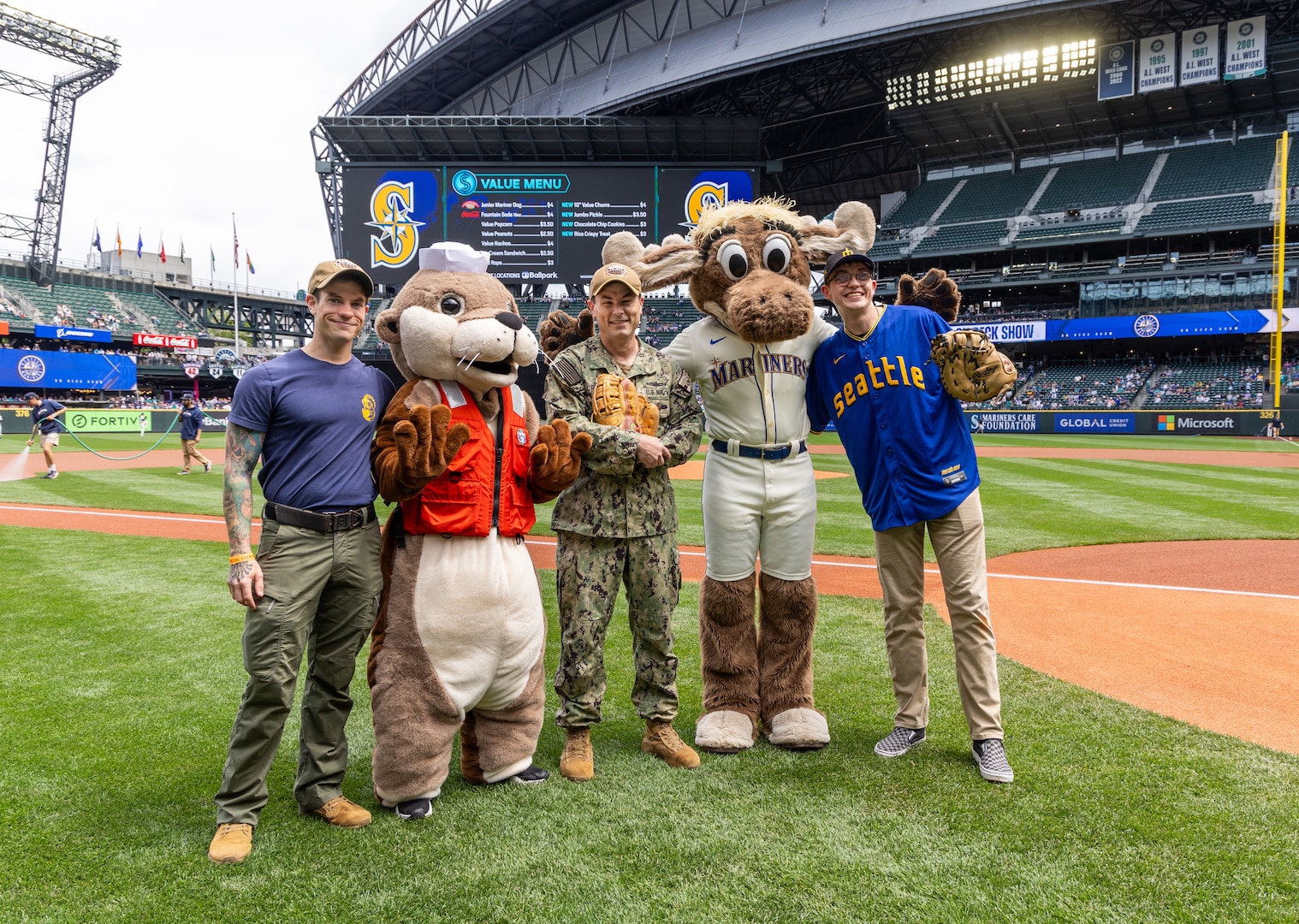 Capt. JD Crinklaw, commander, Puget Sound Naval Shipyard & Intermediate Maintenance Facility, Navy Diver First Class David Loofbourow, Dive Locker, and Zachary Cantrall, dismantler, Shop 75, Dismantling, pose with "Ollie the Otter" and the Mariner Moose June 30, 2024, during pre-game ceremonies at T-Mobile Park in Seattle. (U.S. Navy photo by Wendy Hallmark)