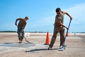 Photo of two Airmen on the flightline using shovels to pick up cement debris.