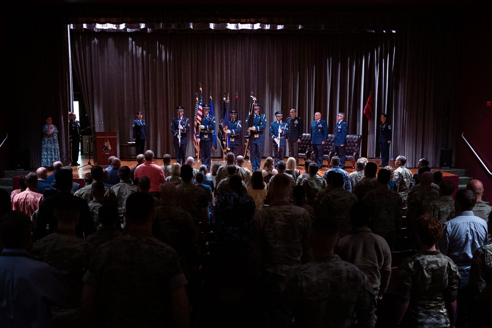 An Honor guard team presents the colors in an auditorium.