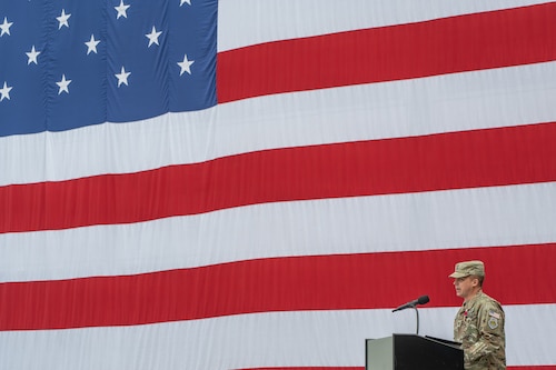 Uniformed military member gives a speech at a podium in front of a US flag during the change of command of space Delta 9.