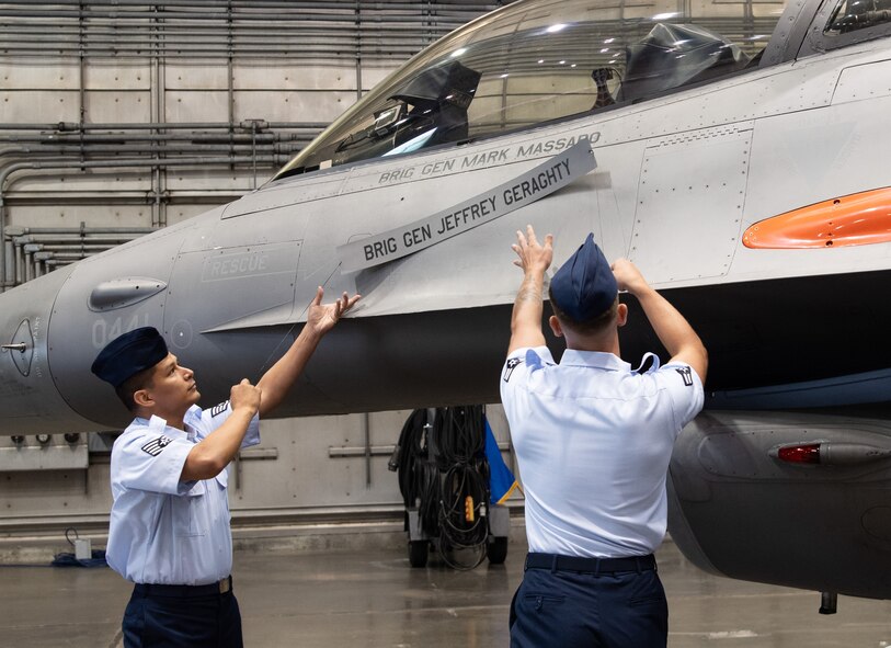 U.S. Air Force Staff Sgt. David Olmeda and Airman 1st Class Jack Lutz, 96th Aircraft Maintenance Squadron, reveal Brig. Gen. Mark Massaro’s name on his F-16 Fighting Falcon during the 96th Test Wing’s change of command inside the McKinley Climatic Lab at Eglin Air Force Base, Fla., July 3, 2024.