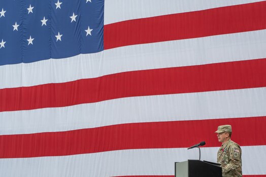  Uniformed military member gives a speech at a podium in front of a US flag during the change of command of space Delta 9.