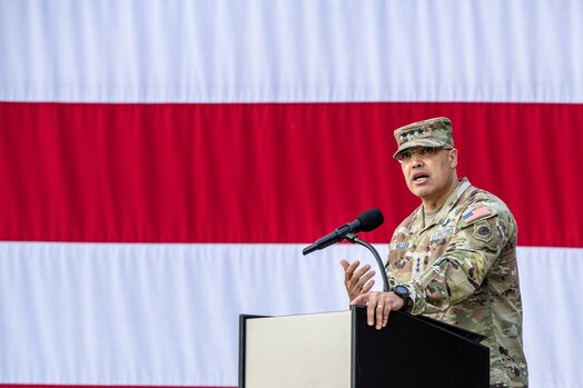  Uniformed member stands at podium and gives a speech in front of the US flag during the change of command of space Delta 9.