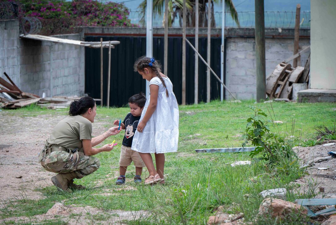 A photo of a military member bending down giving bubbles to children.