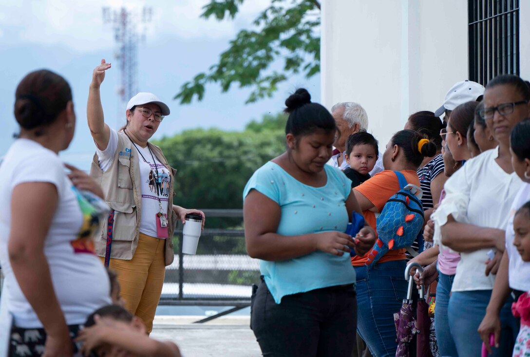 A photo of a woman pointing towards the venue to a group of patients waiting in line.