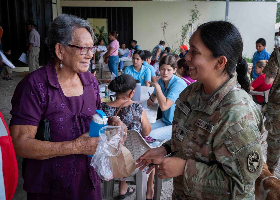 A photo of a military medical professional smiling with a patient after handing her medicine.
