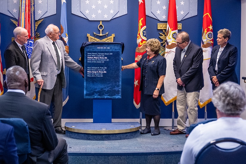 Five people stand on a stage, two pull back a cloth that was draped over a plaque.