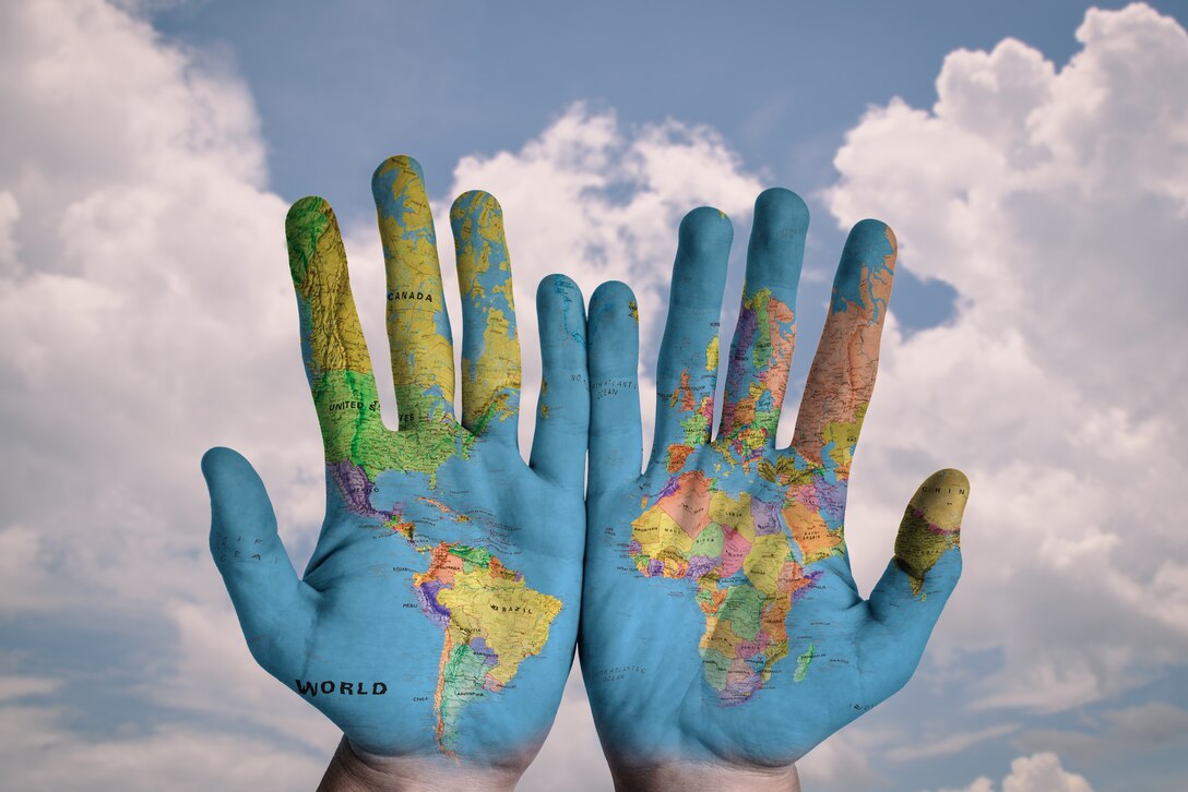 Two hands covered in world map on sky background