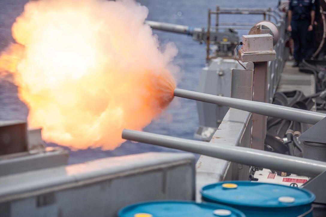 A close-up of a weapon firing, creating a fireball on the side of a ship at sea.