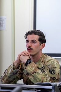 An Army Soldier wearing an Army camouflage uniform is gazing forward during a briefing.