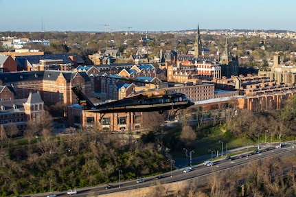 An Army VH-60M "gold top" Black Hawk helicopter flies over Washington, D.C. buildings.