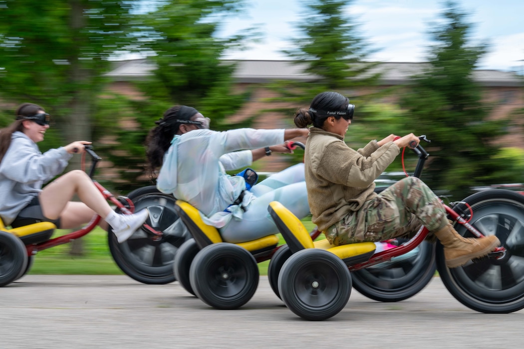 Three airmen wearing goggles ride tricycles with large wheels.