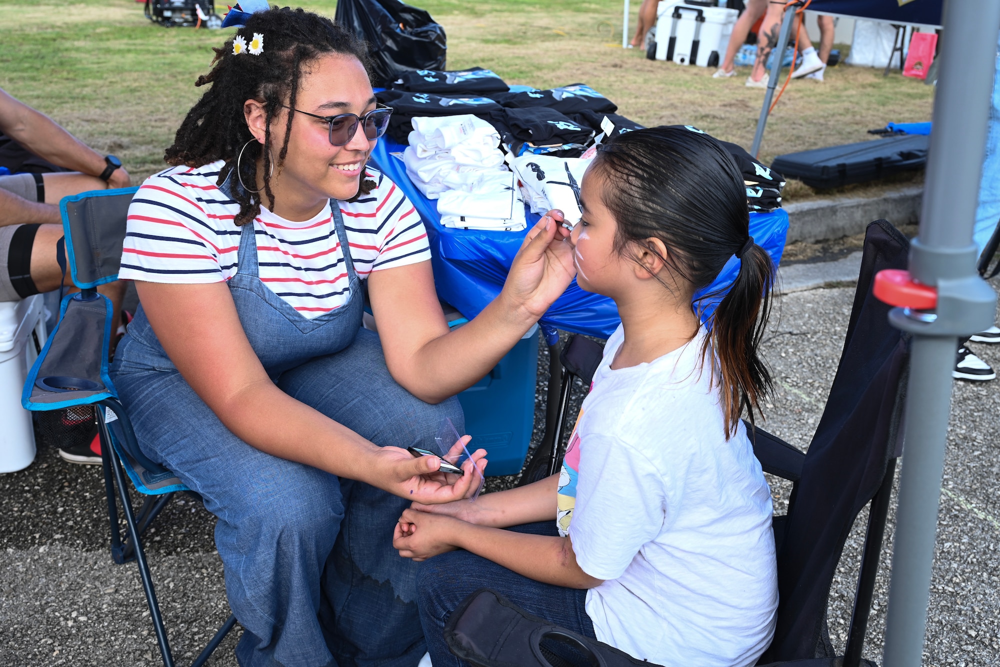 A military member in civilian attire face paints a child of a military  member.