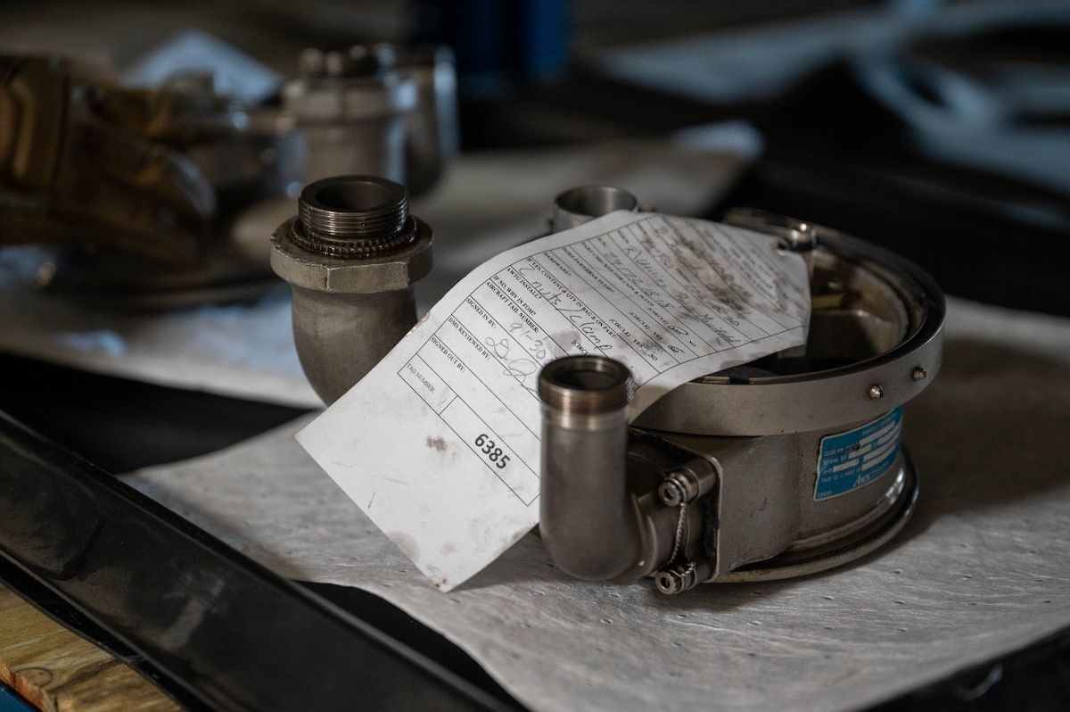 An equipment processing tag is displayed on an F-15E Strike Eagle pump manifold at RAF Lakenheath, England
