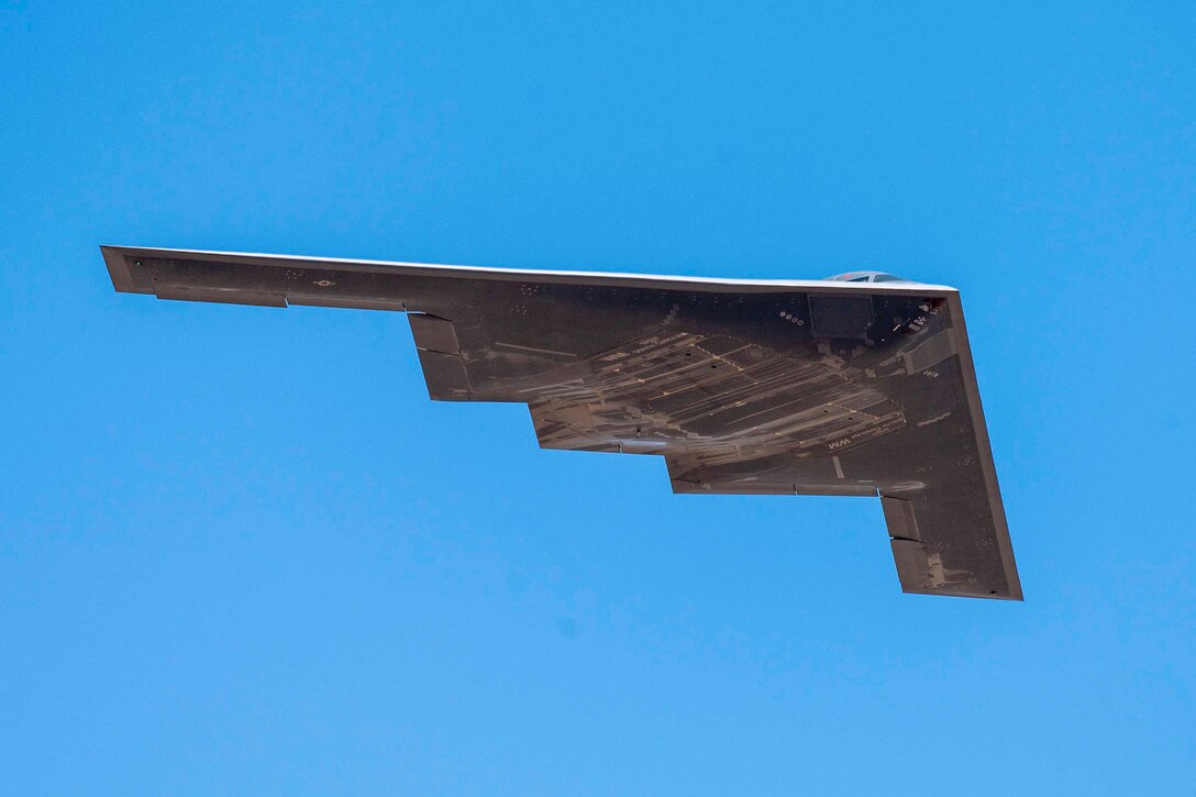 The underside of a bomber is seen as it flies across a blue sky.