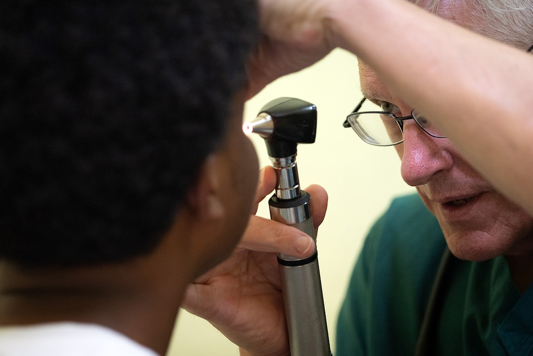 Close-up of a service member using an ophthalmoscope to check the eyes of a patient.