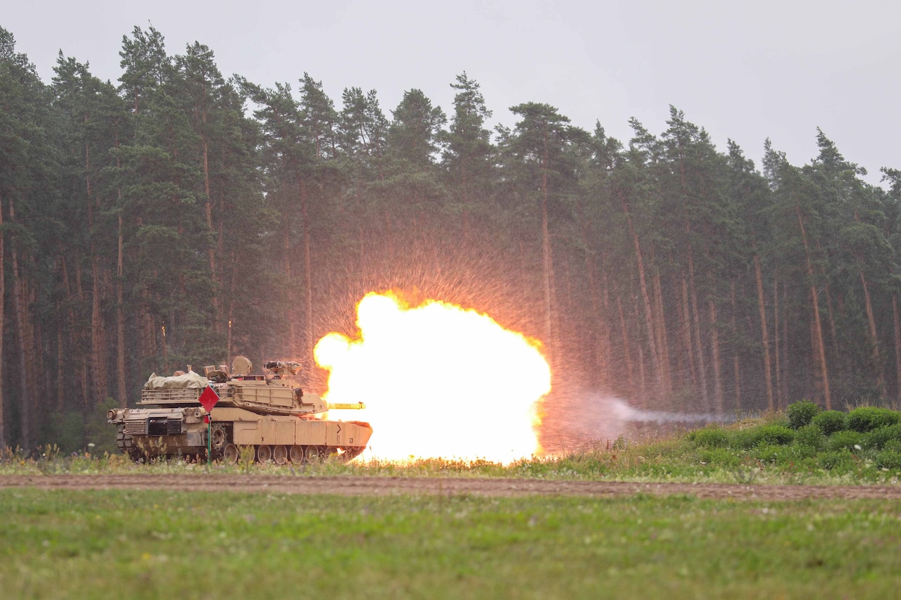 A tank fires a round outside a stand of trees.