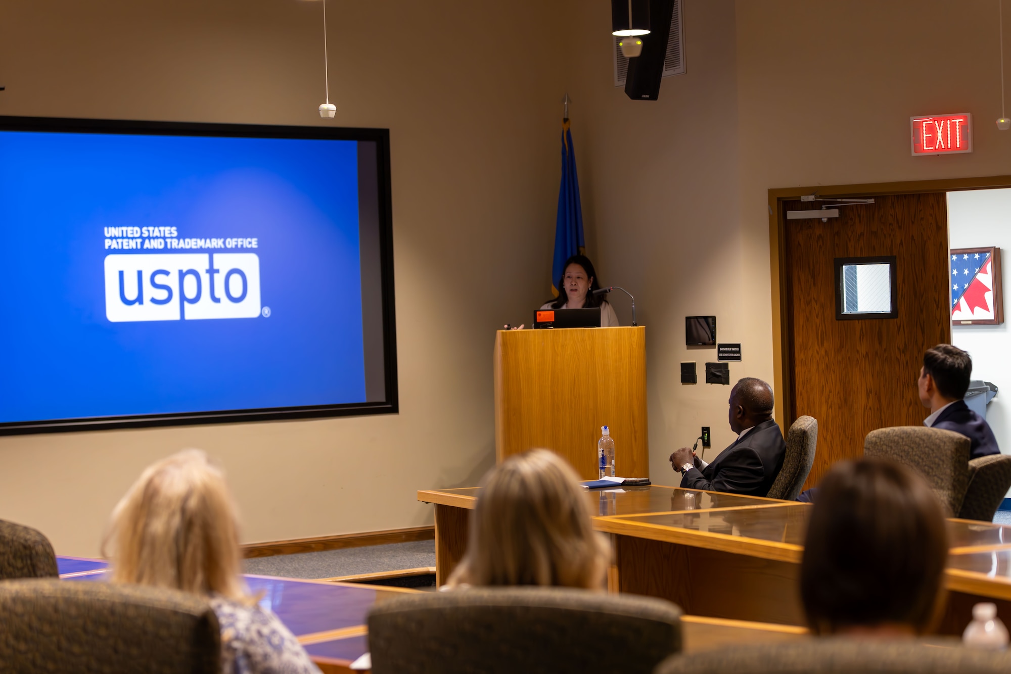 Woman speaking at podium with people at table watching