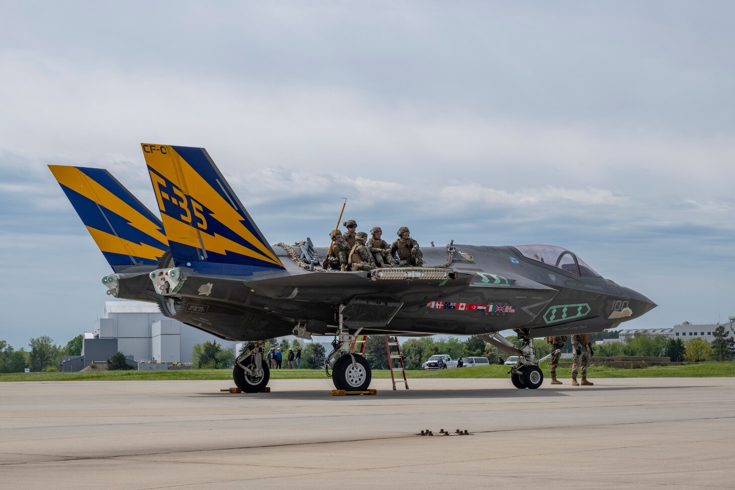 Members of the Helicopter Support Team (HST) from the U.S. Marine Corps Combat Logistics Battalion 26 sit poised atop CF-1, a non-flying F-35C airframe from the NAS Patuxent River F-35 Integrated Test Force, waiting to hook the airframe to sling hoists lowered from a CH-53K being flown by U.S. Marines from VMX-1. The airframe, lifted and transported via CH-53K, was flown from NAS Patuxent River, MD, to Joint Base McGuire-Dix-Lakehurst, NJ, April 24, 2024, to support future testing of emergency recovery systems.