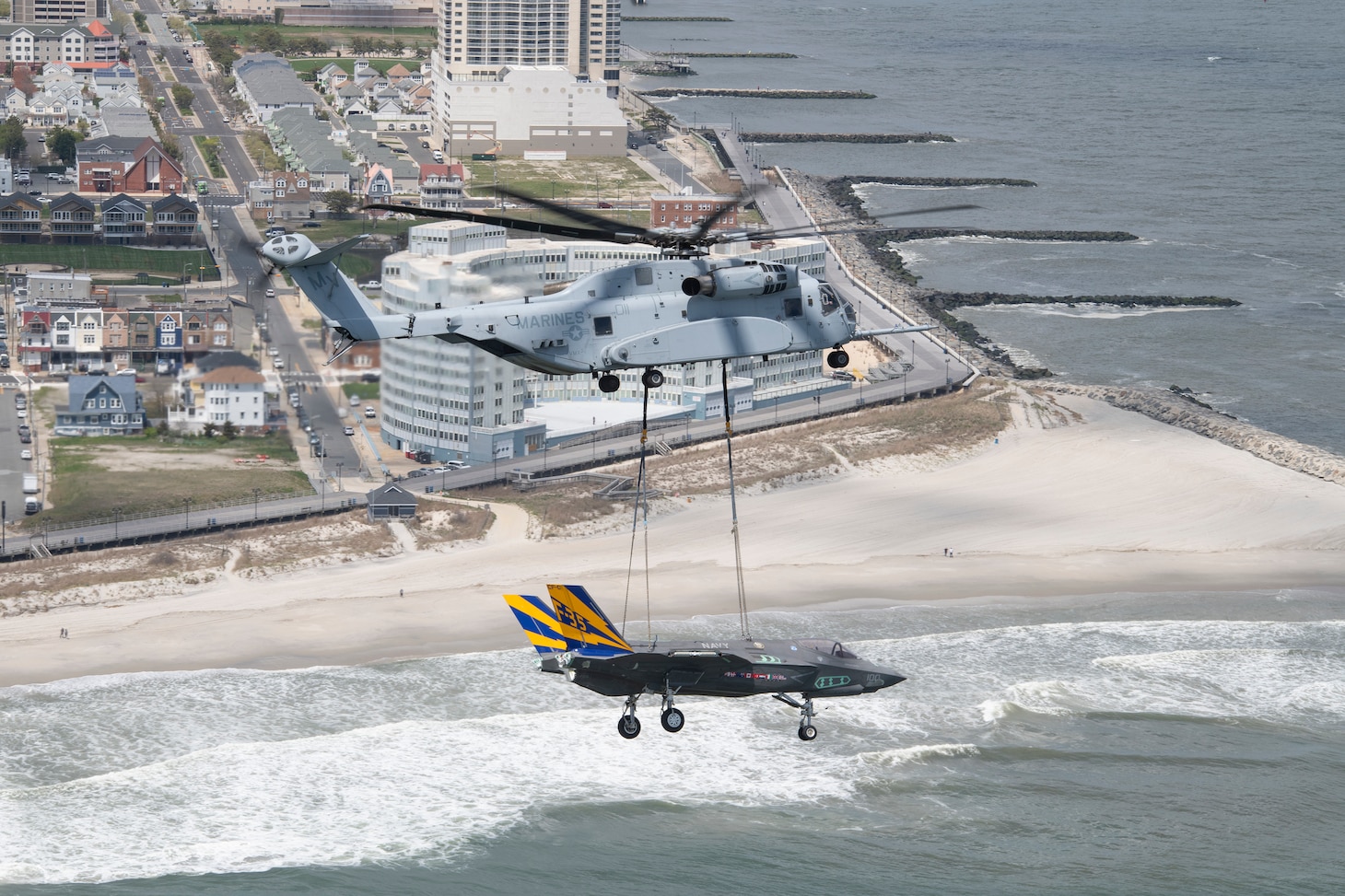 A CH-53K from VMX-1, carrying a non-flying F-35C airframe from the NAS Patuxent River F-35 Integrated Test Force, makes a turn over the Atlantic City coastline in New Jersey as beach-goers stop to watch the unique sight. The April 24, 2024 flight was conducted to transport the non-flying F-35C test airframe from NAS Patuxent River, MD, to Joint Base McGuire-Dix-Lakehurst, NJ, for future testing operations.