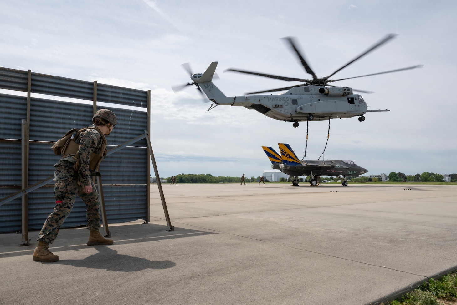 U.S. Marines with the Helicopter Support Team (HST) from Combat Logistics Battalion 26 attach a non-flying F-35C airframe from the NAS Patuxent River F-35 Integrated Test Force to a sling beneath a hovering CH-53K, operated by U.S. Marine Corps pilots from VMX-1, at NAS Patuxent River, MD, April 24, 2024. After being secured to the sling, the airframe was transported via CH-53K to Joint Base McGuire-Dix-Lakehurst, NJ, for use in future testing operations.