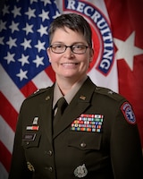 woman wearing U.S. Army uniform standing in front of two flags.