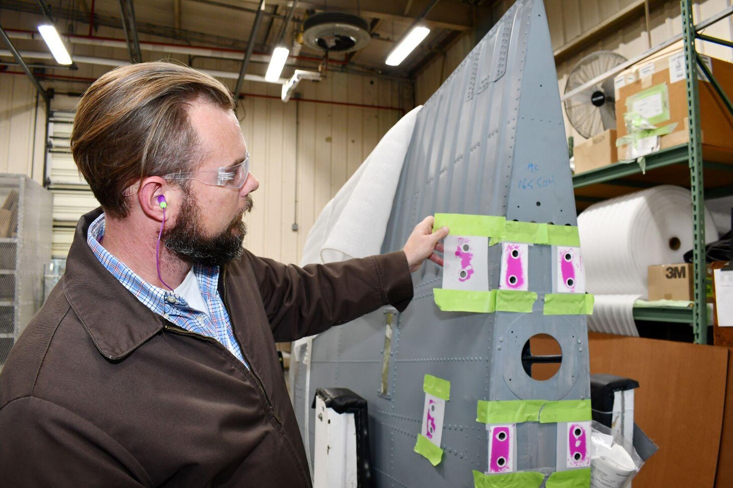 Jason Gaskill, an H-53 airframe production support engineer with the Maintenance, Repair and Overhaul Engineering Production Line Support Division at Fleet Readiness Center East (FRCE), examines successive rounds of impressions left by pressure-sensitive film while checking contact surfaces on the mount feet of an H-53 spar fitting. The use of the pressure-sensitive film to identify high areas on the fitting is part of a new procedure developed and refined by a team of artisans and engineers at FRCE in order to improve the manner in which the aircraft’s spar fittings are evaluated for fit.