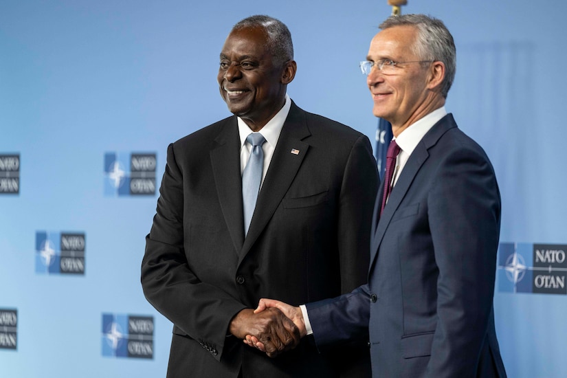 Two civilians shake hands  and smile.