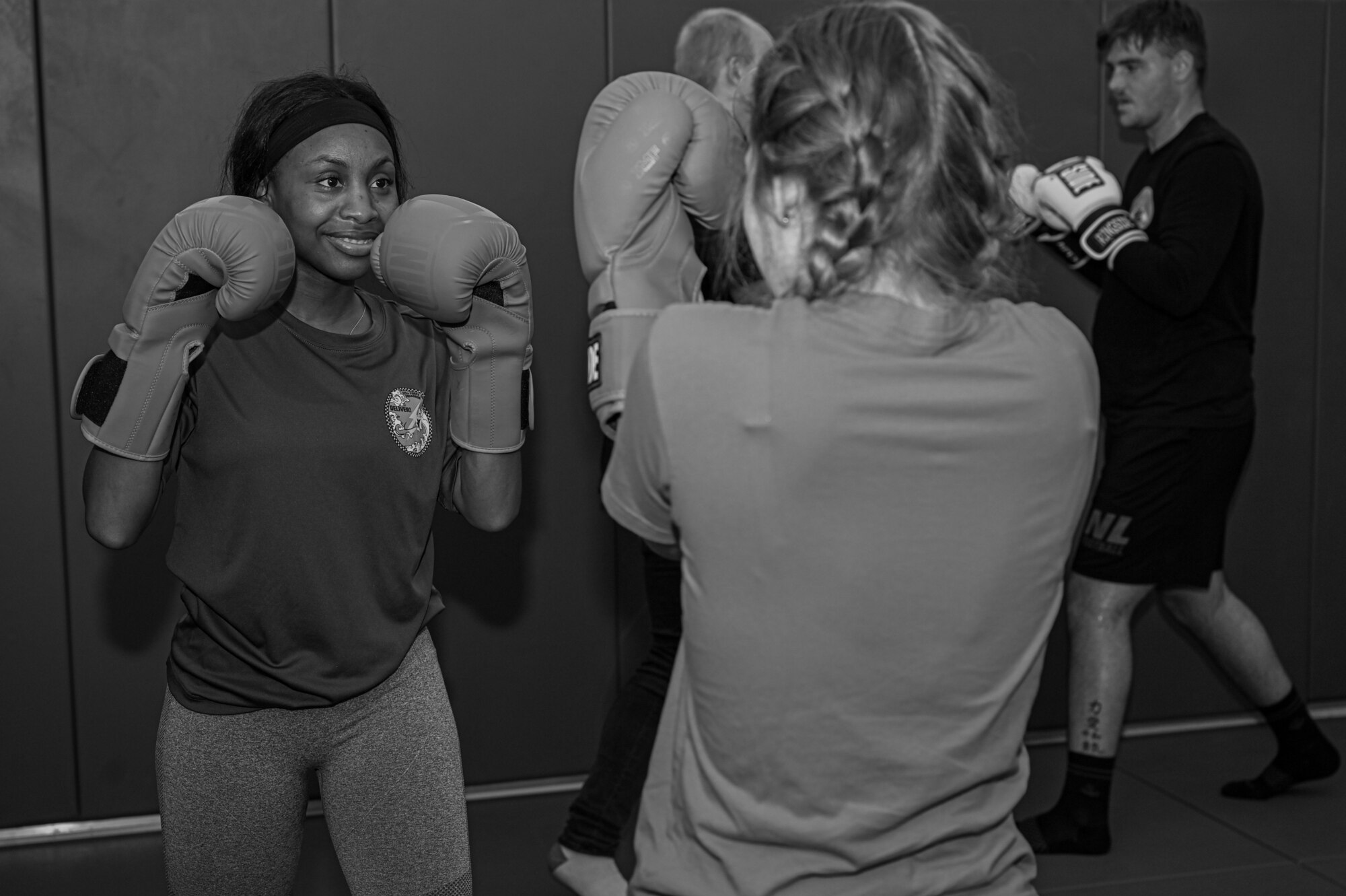 Photo of two students wearing gloves practicing jabs in the foreground and two in the background. Photo in black and white.