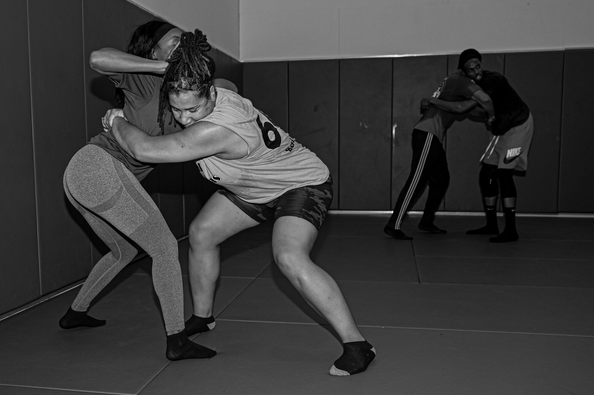 photo of four participants grappling, two in the foreground and two in the background. Photo in black and white.