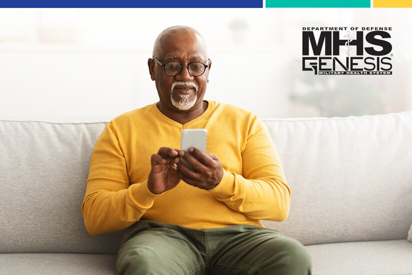 Elderly man wearing glasses sits on couch and looks at smartphone.