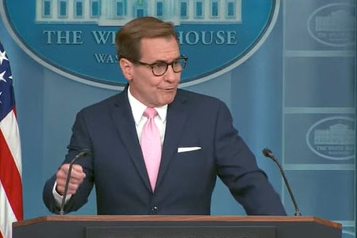 A person wearing a business suit and eyeglasses stands at a lectern.