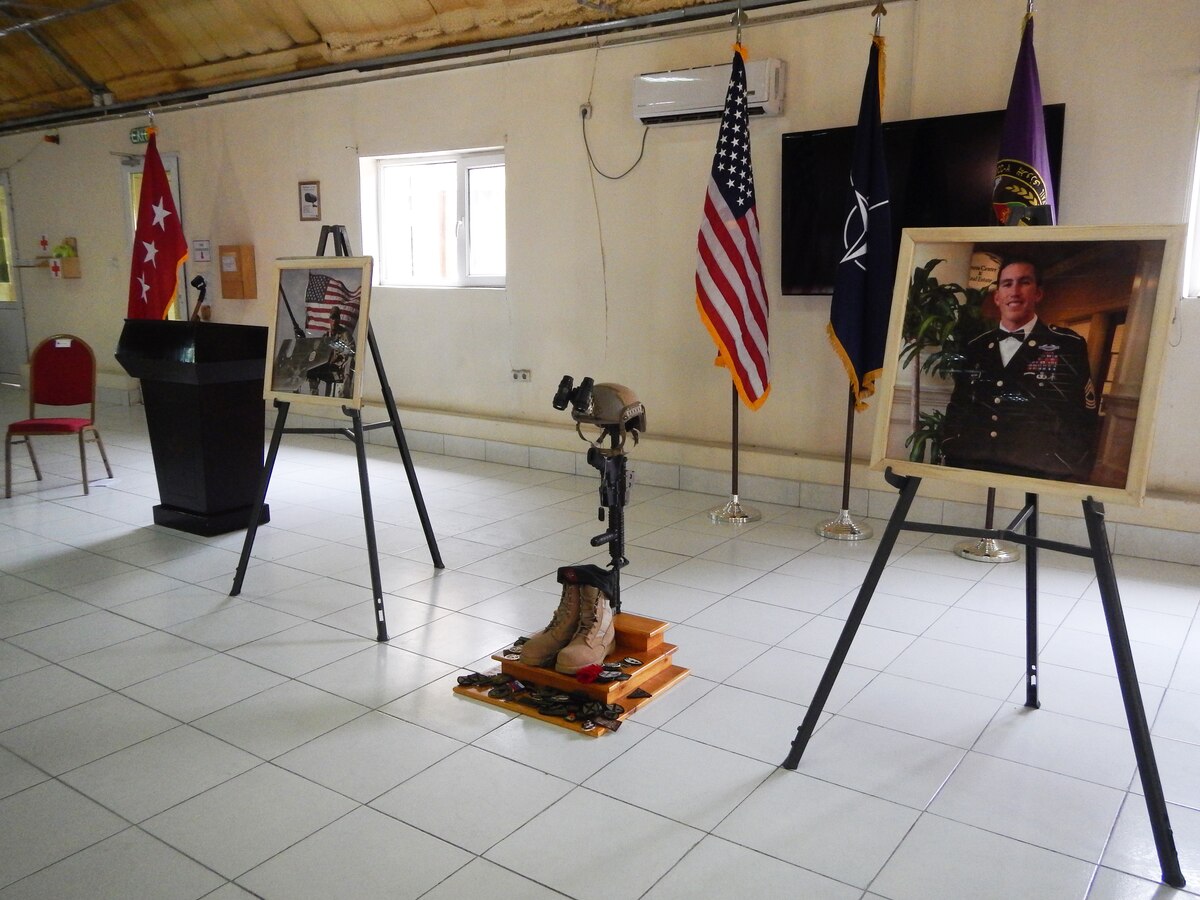 Infantry equipment consisting of a helmet, rifle, boots and I.D. tags, or dog tags, and photos stand at a coalition forces memorial ceremony at Camp Integrity