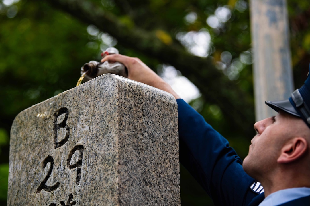 An airman pours bourbon over the top of a stone memorial with “B 29” engraved on the side.