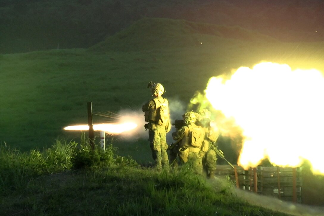 Marines fire a weapon system at night, creating bright yellow fire and smoke.