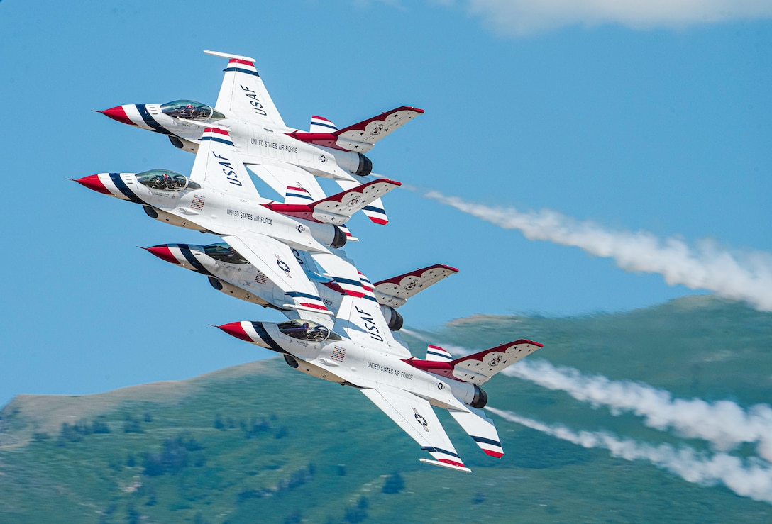 Four Air Force aircraft fly in formation against a bright blue sky, leaving vapor trails.