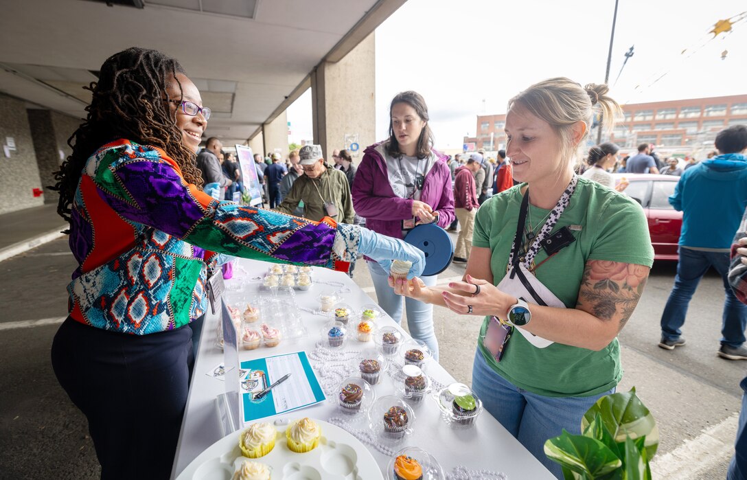 Ashley Jackson, Black, Indigenous and People of Color Employee Resource Group co-lead, serves cupcakes to employees, including Dianna Carlson, supervisor, Code 105.3, Radiological Controls Technicians, at the "Cupcake Wars" booth June 27, 2024, during a command's "Pathway To Safety" training event at Puget Sound Naval Shipyard & Intermediate Maintenance Facility in Bremerton, Washington. (U.S. Navy photo by Wendy Hallmark)